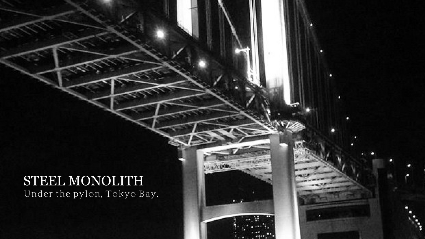 STEEL MONOLITH artwork: black-and-white view of a massive bridge structure under night lights near Tokyo Bay.